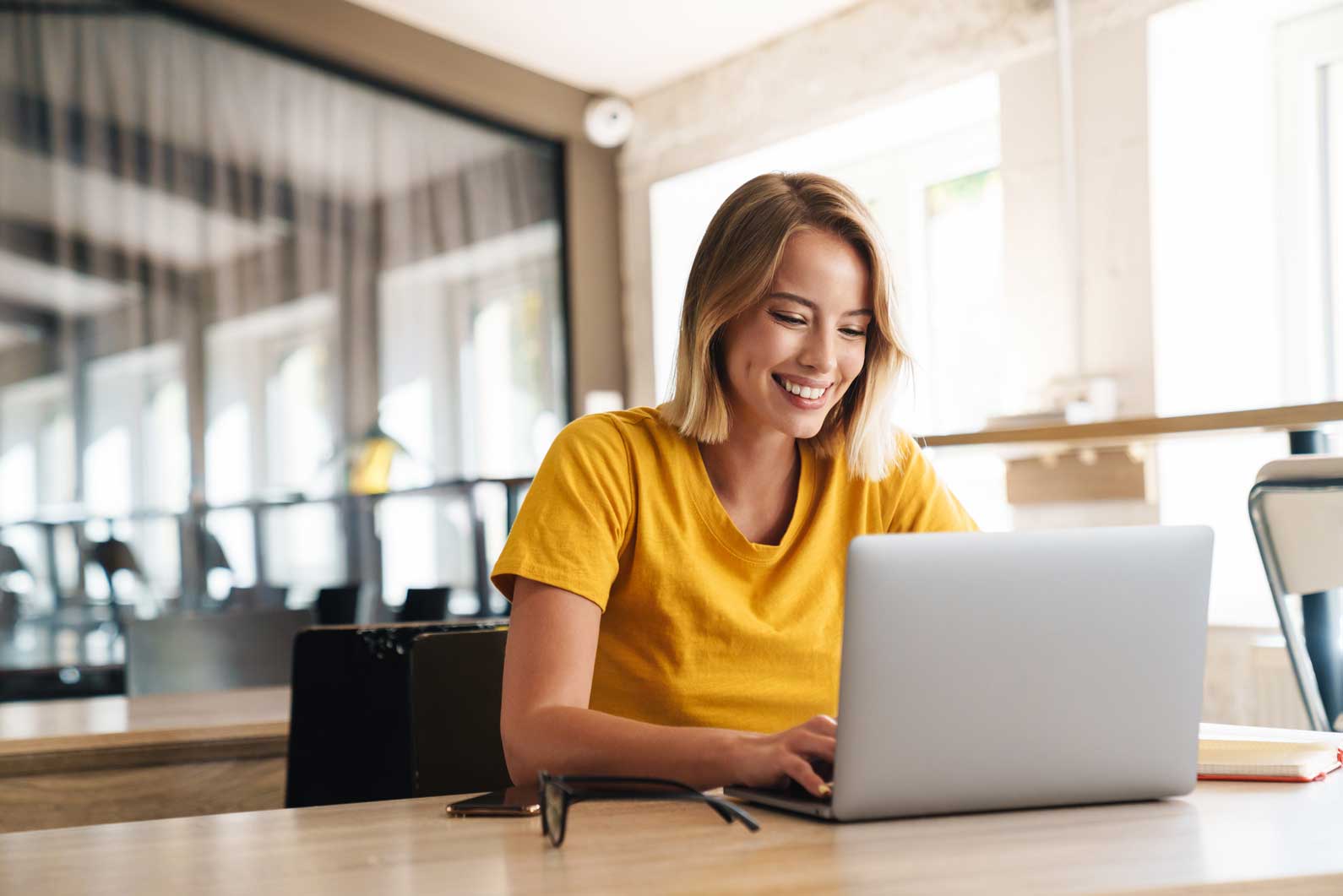 a woman in an orange t-shirt sits at a laptop working