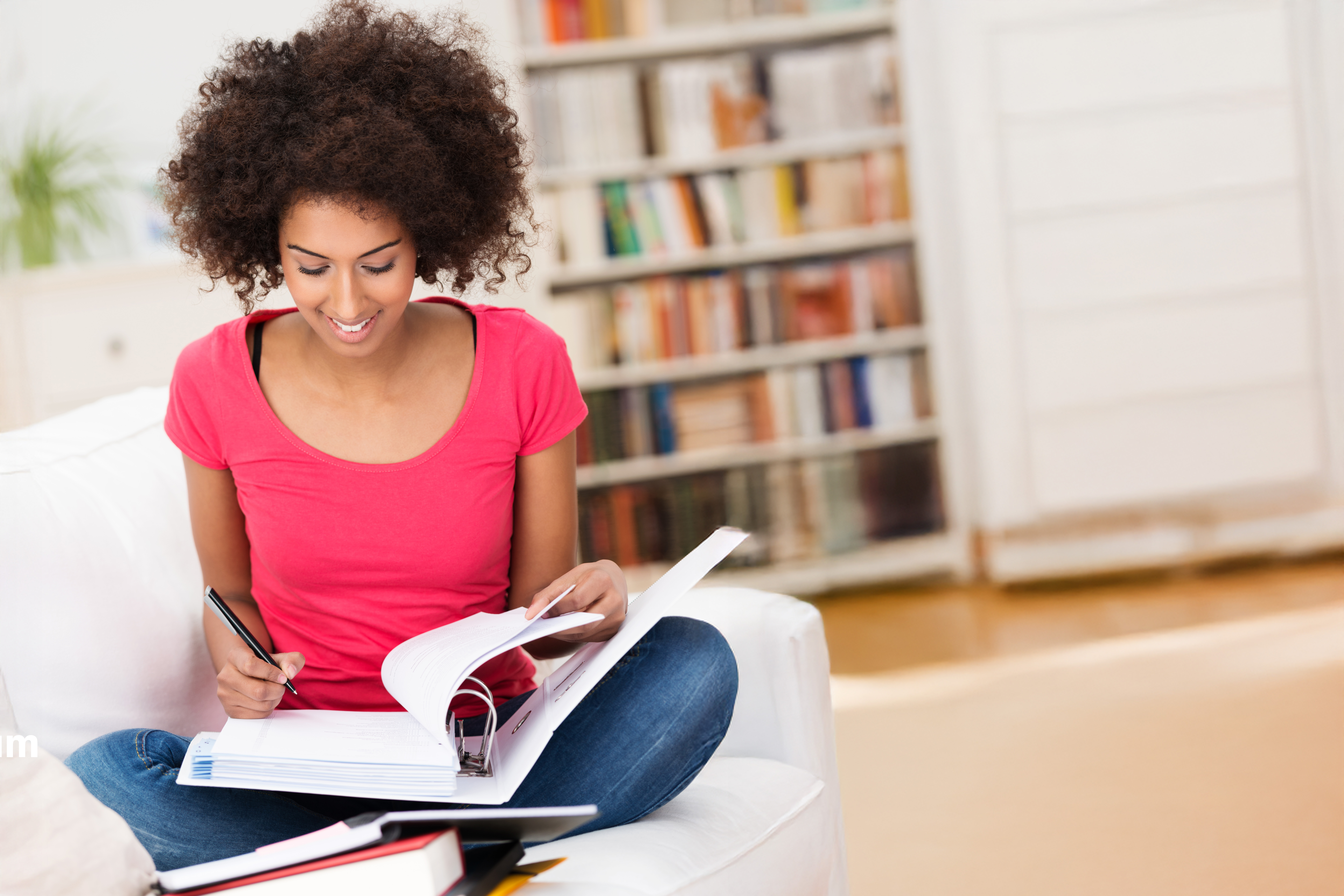 Eine junge Frau sitzt auf einer Couch im Schneidersitz und studiert Dokumente