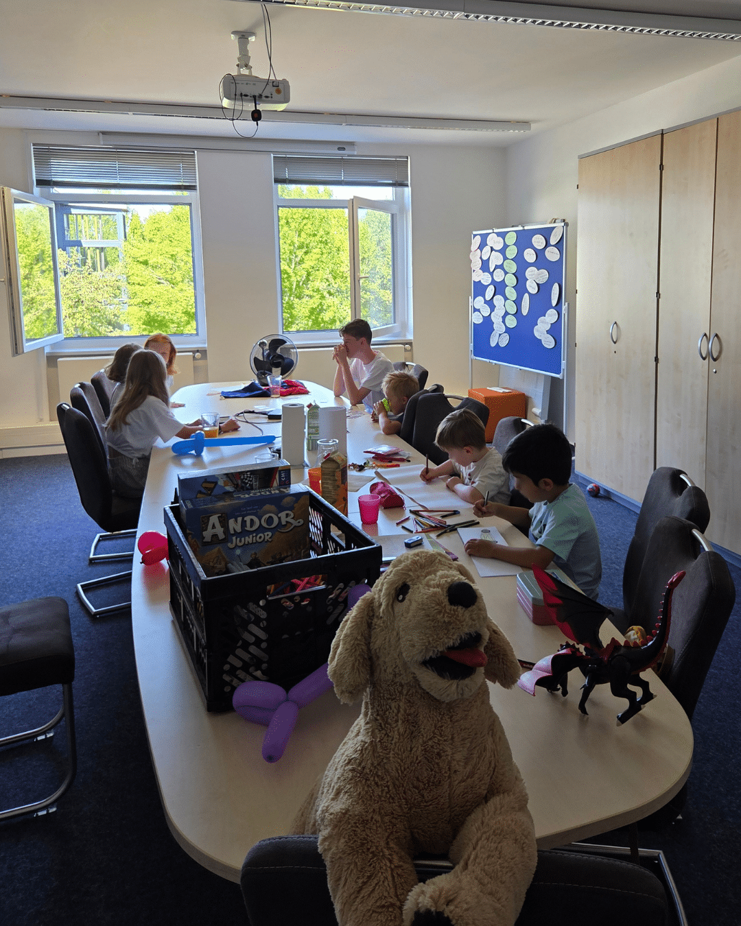 Viele Kinder sitzen an einem großen Tisch und sind am Malen, Reden und Spielen