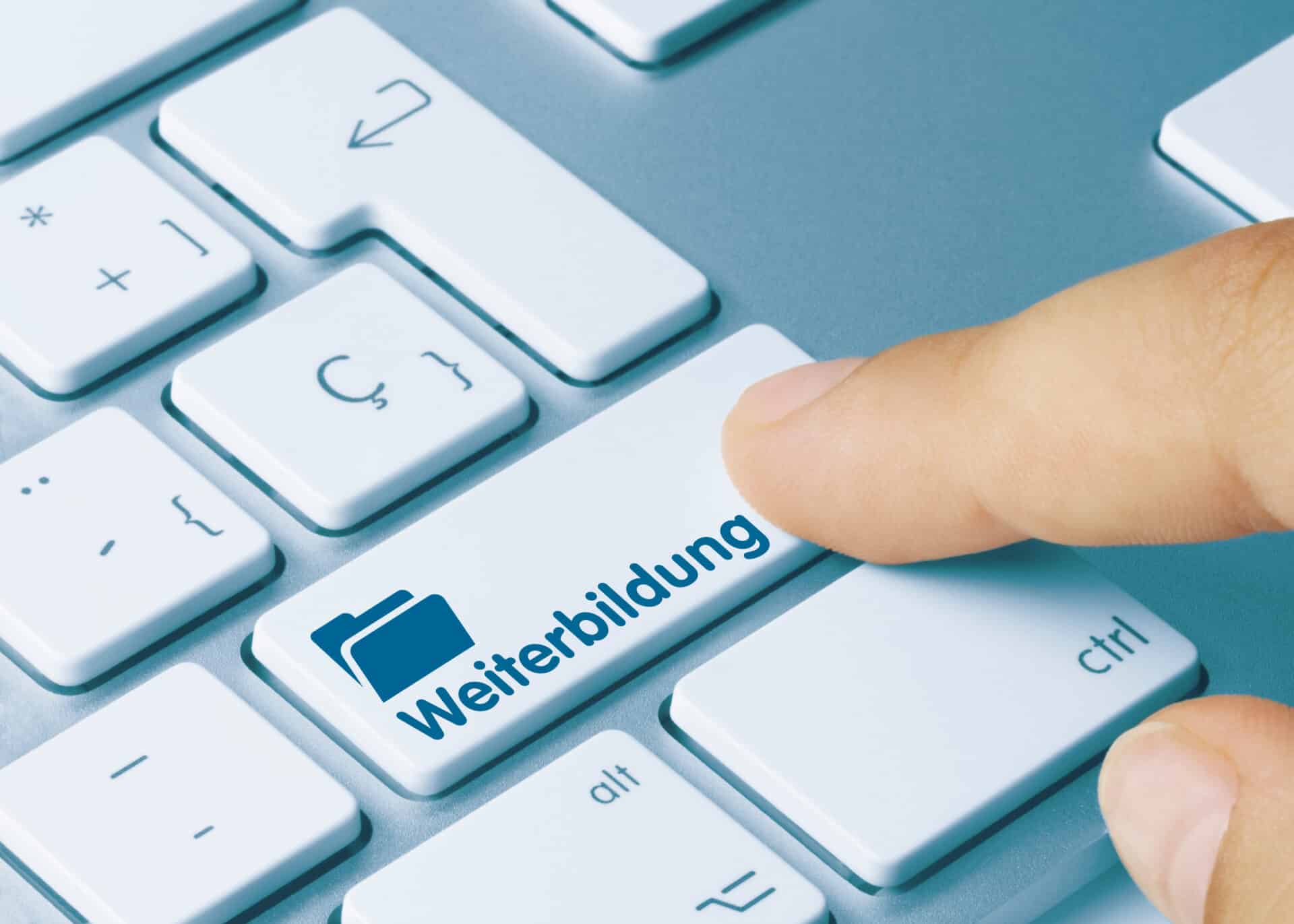 Ein Ausschnitt einer Tastatur, bei der ein Finger auf eine Taste mit dem Text Weiterbildung klickt