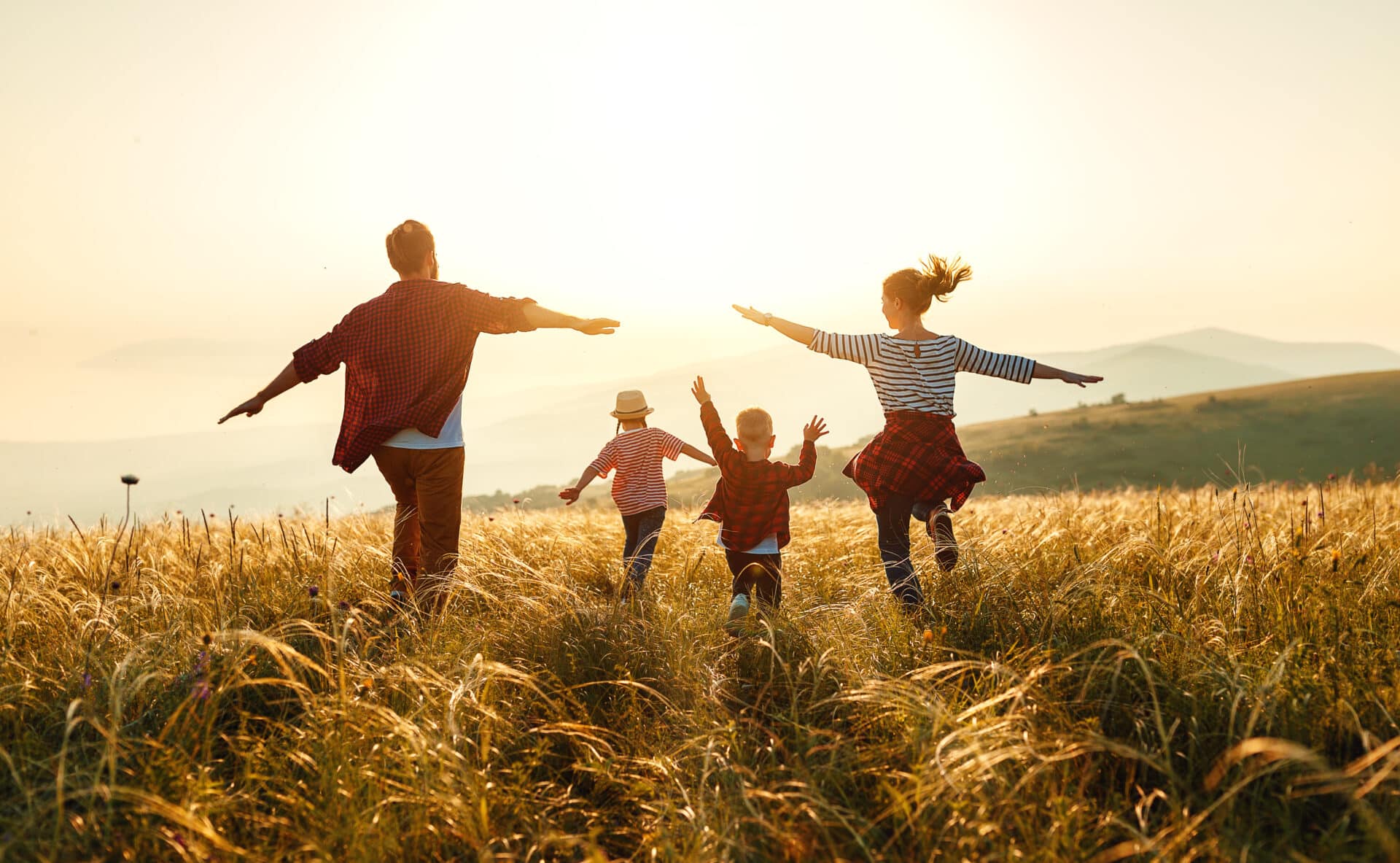 Bild zeigt eine glückliche Familie die über das Feld Richtung Sonne läuft